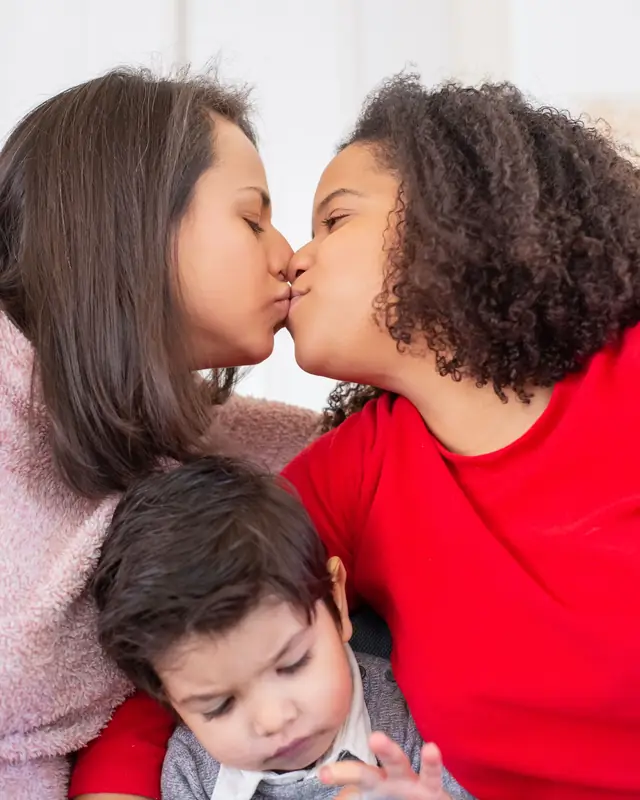 Two mothers share a kiss while their little boy sits between them