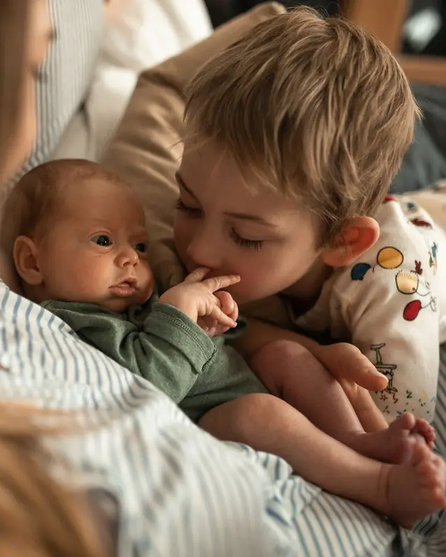 A little boy kisses the hand of a newborn held in a parent's arms
