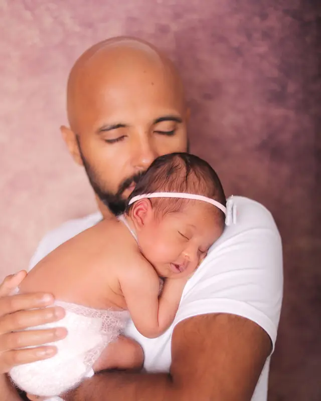 A father holds his sleeping newborn daughter against his chest, eyes closed
